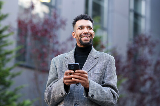 Smiling man in suit with smartphone on city street, low angle view