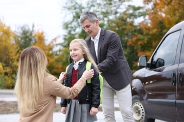 Parents taking their daughter to school near car outdoors