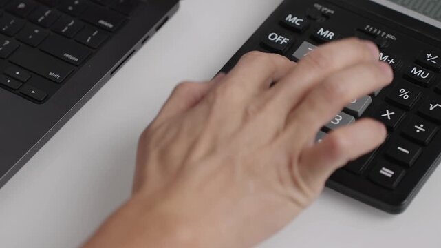 Close up of calculator and laptop neatly arranged on light desk. Student fingers hitting buttons of calculator. Unrecognized person building financial budget. Accountant counts taxes. - Powered by Adobe