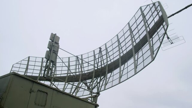 curved radar antenna atop military rooftop under overcast sky, large parabolic mesh array mounted on olive