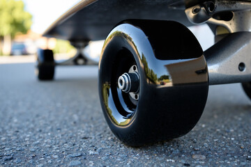 Extreme close-up macro shot of a black skateboard wheel resting on rough asphalt pavement, with the deck blurred in the background. Urban sports, youth culture, and the skateboarding lifestyle