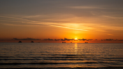 Golden hour sunset over calm sea with ships on the horizon – serene ocean seascape background