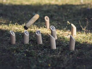 A Molkky throwing pin is caught mid-air as it strikes numbered skittles on grass. This Finnish outdoor game combines precision, strategy, and family-friendly fun.