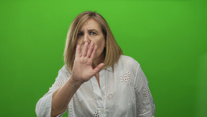 Woman raises hand and gestures with both hands in studio with green screen while wearing serious expression; warning.