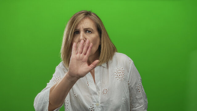 Woman raises hand and gestures with both hands in studio with green screen while wearing serious expression; warning.