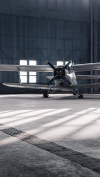 Front view of an old propeller aircraft in a hangar. 9x16 vertical image of white biplane aircraft in roomy sunlit hangar.
