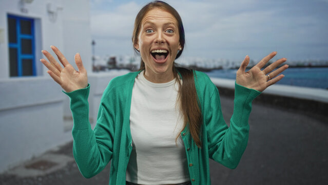 Young woman making hand binoculars on seaside promenade, hands framing eyes and smiling in green cardigan and crop top; joyful.