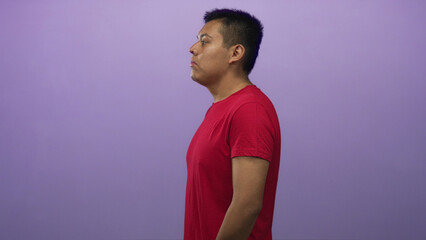 Hispanic man standing in purple studio in side profile, wearing red t shirt with visible face and...