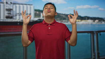 Man making ok sign with hands on ship building deck wearing red polo with eyes closed; serenity...