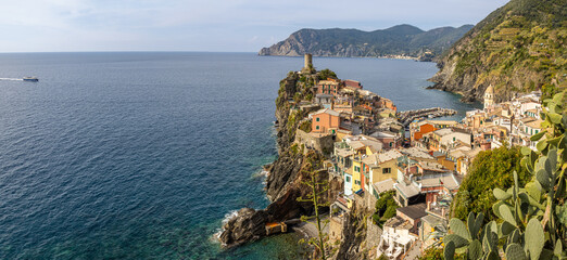 A panorama of Vernazza captured from the path towards Corniglia, with the Doria castle tower dominating the cliff and colorful houses clustered around the port. Cinque Terre, Italy