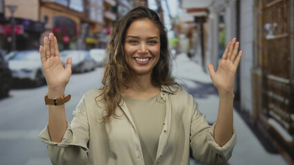 Woman raises both hands in a wide size gesture on a bright sunlit street outdoors; scale...