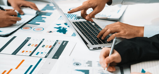 A diverse business team collaborates on a digital marketing strategy. Laptops and documents filled with data, charts, and graphs fill the modern office space. SACTR