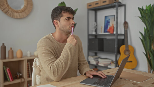 Man works on laptop typing in home office while young hispanic guy sketches ideas in notebook on desk with pen.