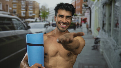 Man with bare chest holding a blue yoga mat and extending his hand on a city street; encouragement motivation energy.
