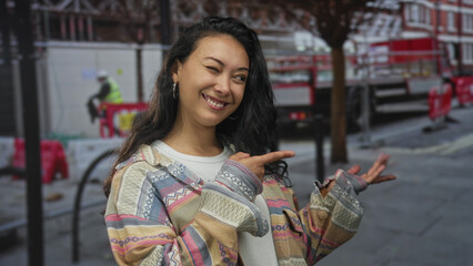 Woman pointing finger toward scaffolding at construction site on street, smiling directly at camera; joy.
