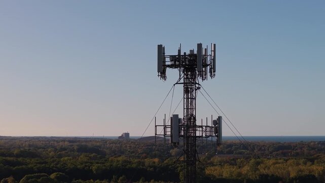 Close-up view of a telecommunication tower above a forest landscape near a lake under a clear blue sky