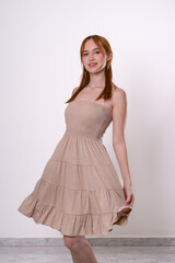 Red-haired woman smiling in beige dress, joyful and confident studio fashion portrait.