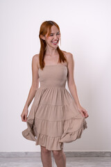 Naklejka premium Red-haired woman posing in beige dress with slight movement, graceful and natural studio portrait.
