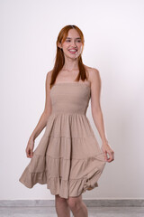 Red-haired woman spinning softly in beige dress, joyful and carefree studio portrait.