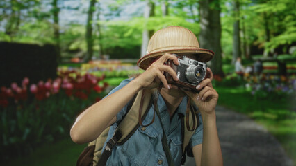 Woman explorer with backpack lifts camera to eyes in forest path capturing vibrant greenery and...