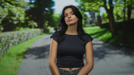 Fototapeta premium Woman midriff tilts head by stone wall along forest lane under soft sunlight haze; confidence reflection.