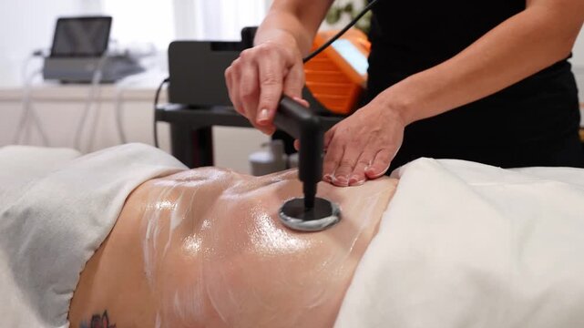Professional beautician performing an aesthetic radiofrequency treatment on a client's abdomen for body shaping and skin tightening