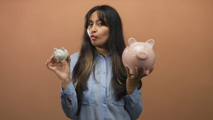 Woman holding a large pink piggy bank and a small white piggy bank, puckering lips in a peach...