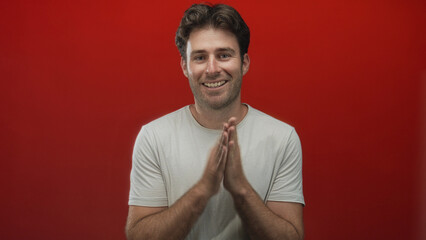 Man clapping hands and smiling in a red studio, wearing a white t shirt with visible forearms and...