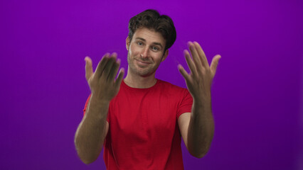 Man points finger to camera and shows thumbs gesture wearing red t shirt in purple studio; playful confidence.