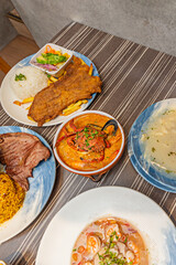 The traditional La Paz-style hornado features juicy roasted pork with crispy skin, accompanied by corn tortillas, hominy, and llapingachos (potato pancakes) smothered in peanut sauce