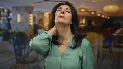 Middle aged hispanic woman with hand on neck gesture and closed eyes in a hotel lobby building...