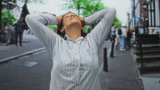 Woman with hands on head and striped shirt standing on a busy city street with bicycles and pedestrians visible; relief. - Powered by Adobe