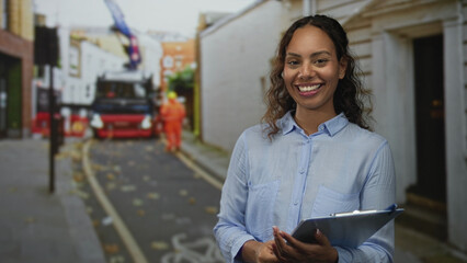 Woman holding clipboard covering mouth with hand on a busy city street beside a parked truck and workers in orange vests, smiling in surprise; friendly amusement.