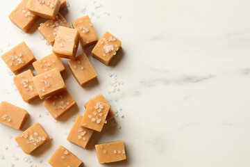 Tasty caramel candies with salt on light marble table, flat lay. Space for text