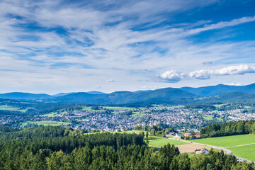 Fototapeta premium Bright panoramic view of a small town surrounded by forests, fields, and distant blue mountains.