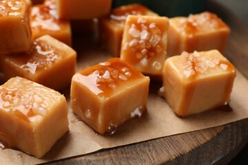 Tasty candies with salt and caramel sauce on wooden board, closeup