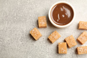 Tasty candies with salt and caramel sauce on grey textured table, flat lay. Space for text