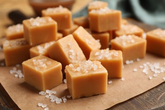 Tasty caramel candies with salt on wooden board, closeup