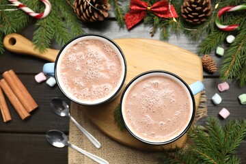 Tasty hot cocoa drink in mugs, marshmallows and Christmas decor on dark wooden table, flat lay