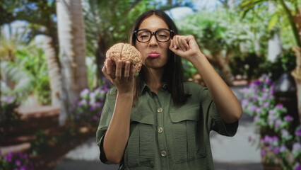 Woman brunette wearing glasses and green shirt holds anatomical brain model in hand and rubs eye...