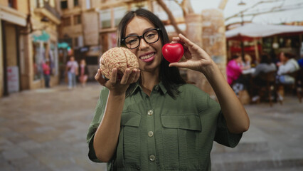 Hispanic woman holding a brain model in her left hand and a red heart in her right hand on a street...