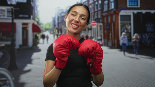 Woman holds boxing gloves up in a street boxing stance, smiling and posing with red mitts; confidence training empowerment.