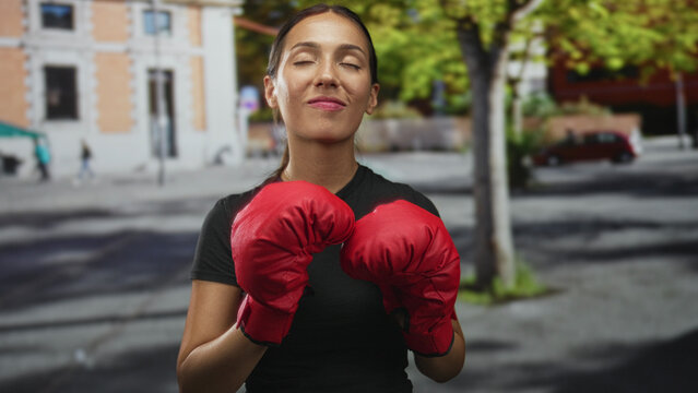 Woman holding red boxing gloves with fists raised on a street in front of a building; confidence resilience empowerment.