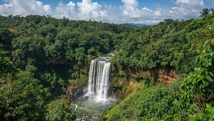 Lush green landscape surrounding a waterfall cascading into a river. Dense forest with vibrant foliage. Scenic nature scene with a waterfall and greenery.