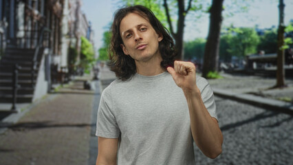 Fototapeta premium Young hispanic man with long hair raising right fist and looking at camera in a city street; confidence defiance determination.