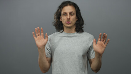 Man, hispanic and young, with long hair raising hands showing palms and neutral expression in...
