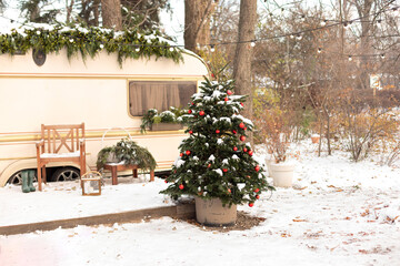 Christmas-themed winter campsite with a festive RV trailer, outdoor firepit, armchair, snow-covered yard, Xmas holiday tree and cozy garden furniture. Exterior Seasonal mobile home getaway. New Year	
