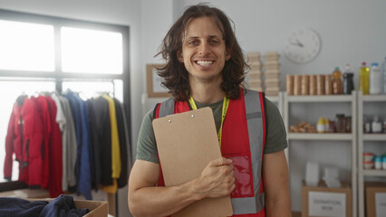 Man holding clipboard and smiling while wearing a volunteer vest in a donation building with coats...