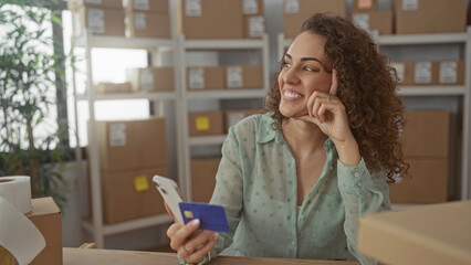 Woman with hands holding a creditcard and smartphone, tapping the screen and smiling while packing...