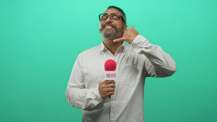 Man holding microphone and making a phone hand gesture in studio with teal backdrop; friendly banter.